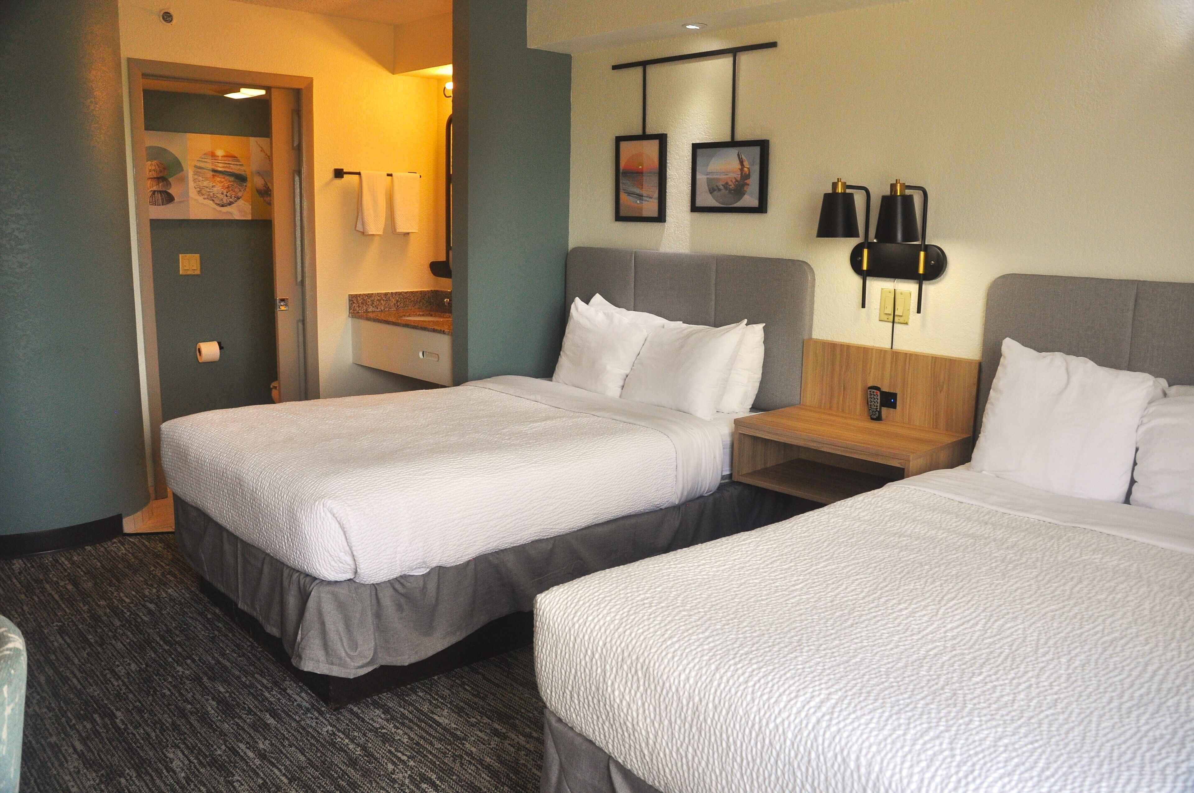 A hotel room with two beds, a bathroom, and a small desk with a lamp.