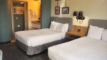 A hotel room with two beds, a bathroom, and a small desk with a lamp.