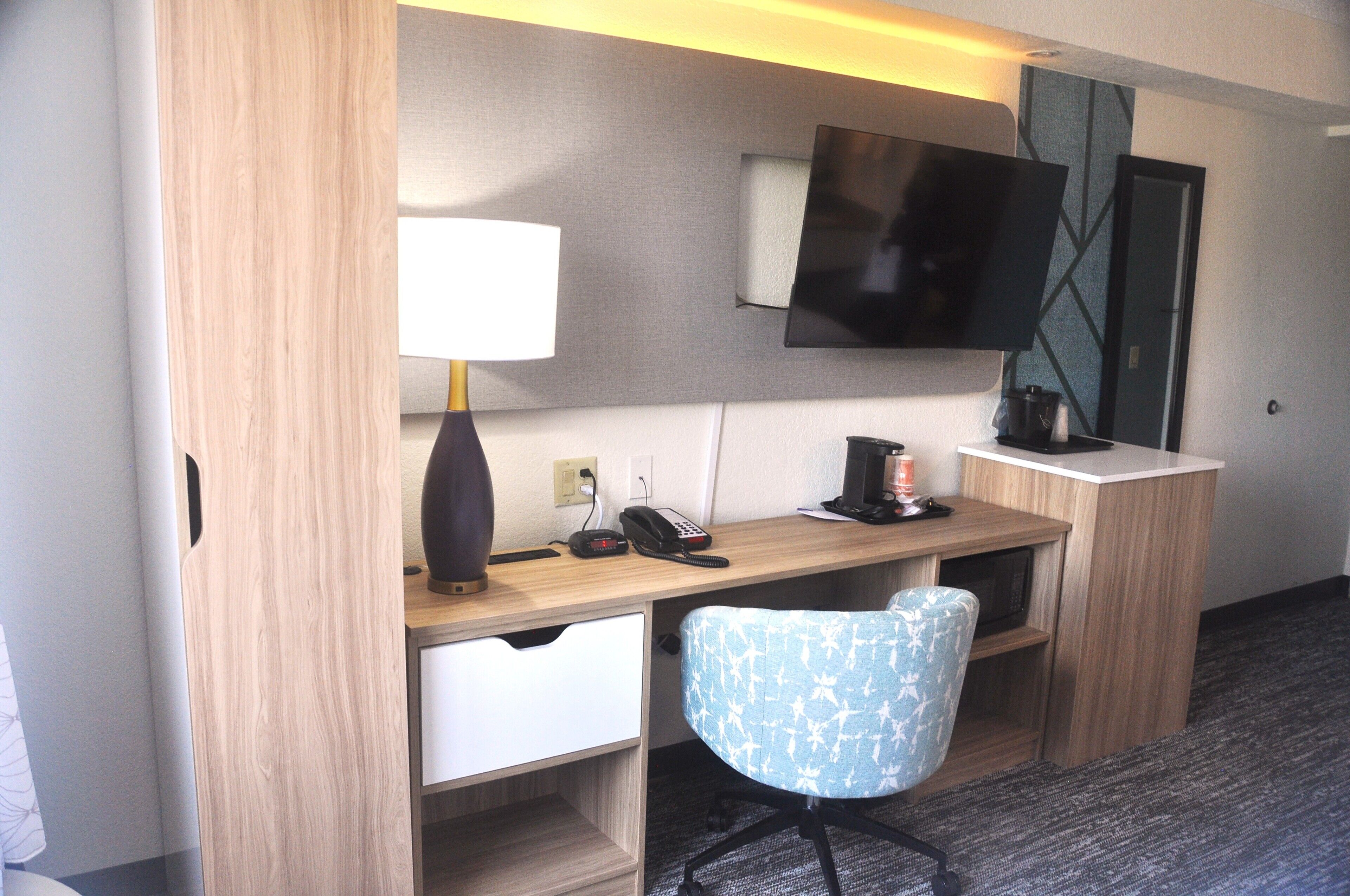 Habitación de hotel con escritorio, silla, lámpara, teléfono y televisor de pantalla plana montado en la pared.