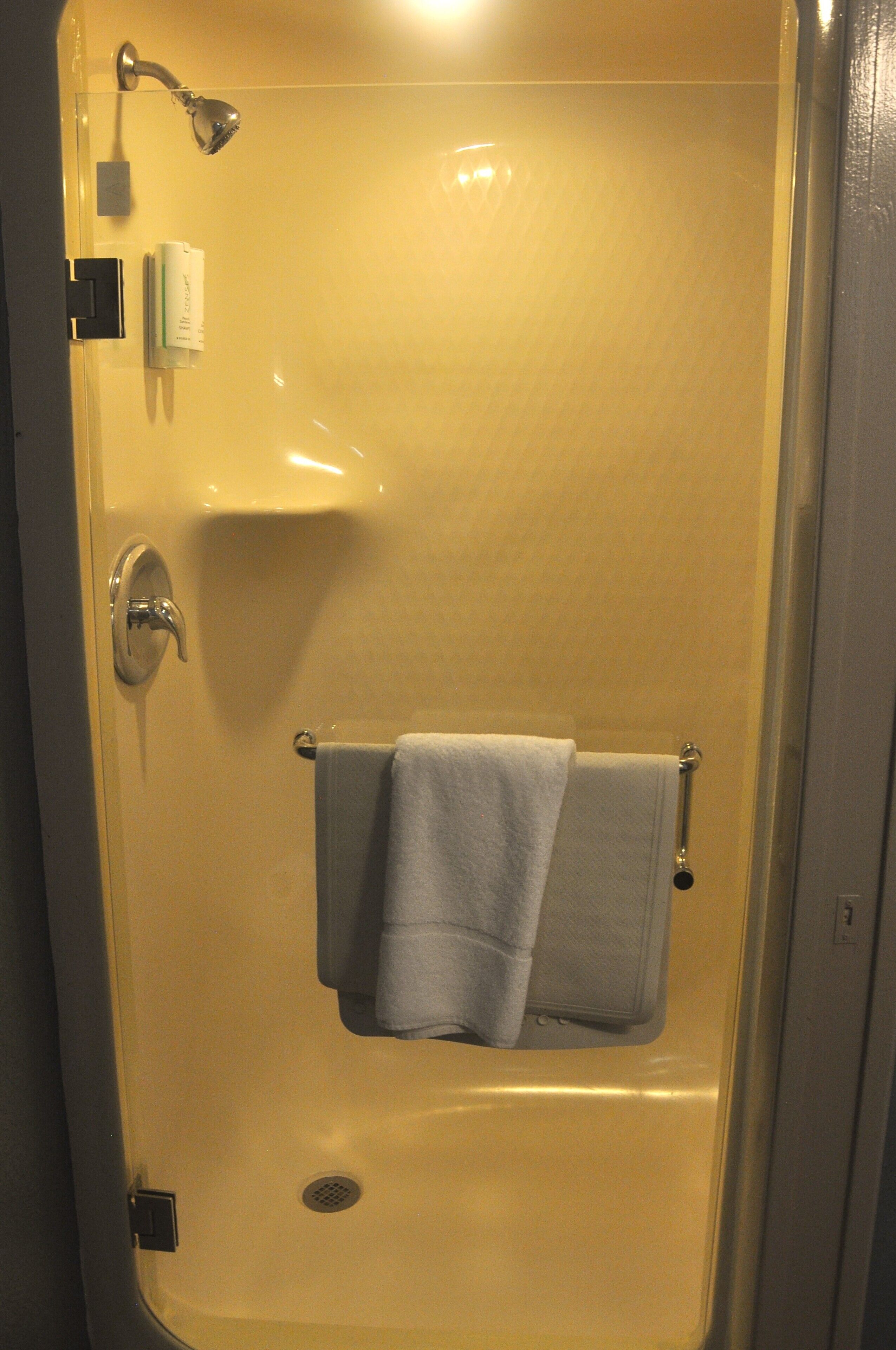 A bathroom with a bathtub, a towel rack with two towels, a handheld showerhead, and a toilet paper holder.