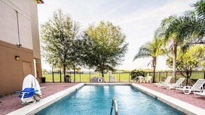 A rectangular swimming pool with a metal ladder, surrounded by a brick walkway, trees, and white lounge chairs. - Sleep Inn Fort Pierce I-95 (Fort Pierce)
