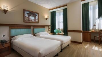 Una camera d'hotel con due letti, una scrivania, una sedia, un telefono e un quadro appeso al muro.