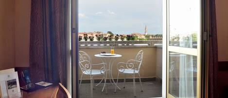 A balcony with a table and chairs, a small round table with a glass of juice, and a bowl of strawberries.