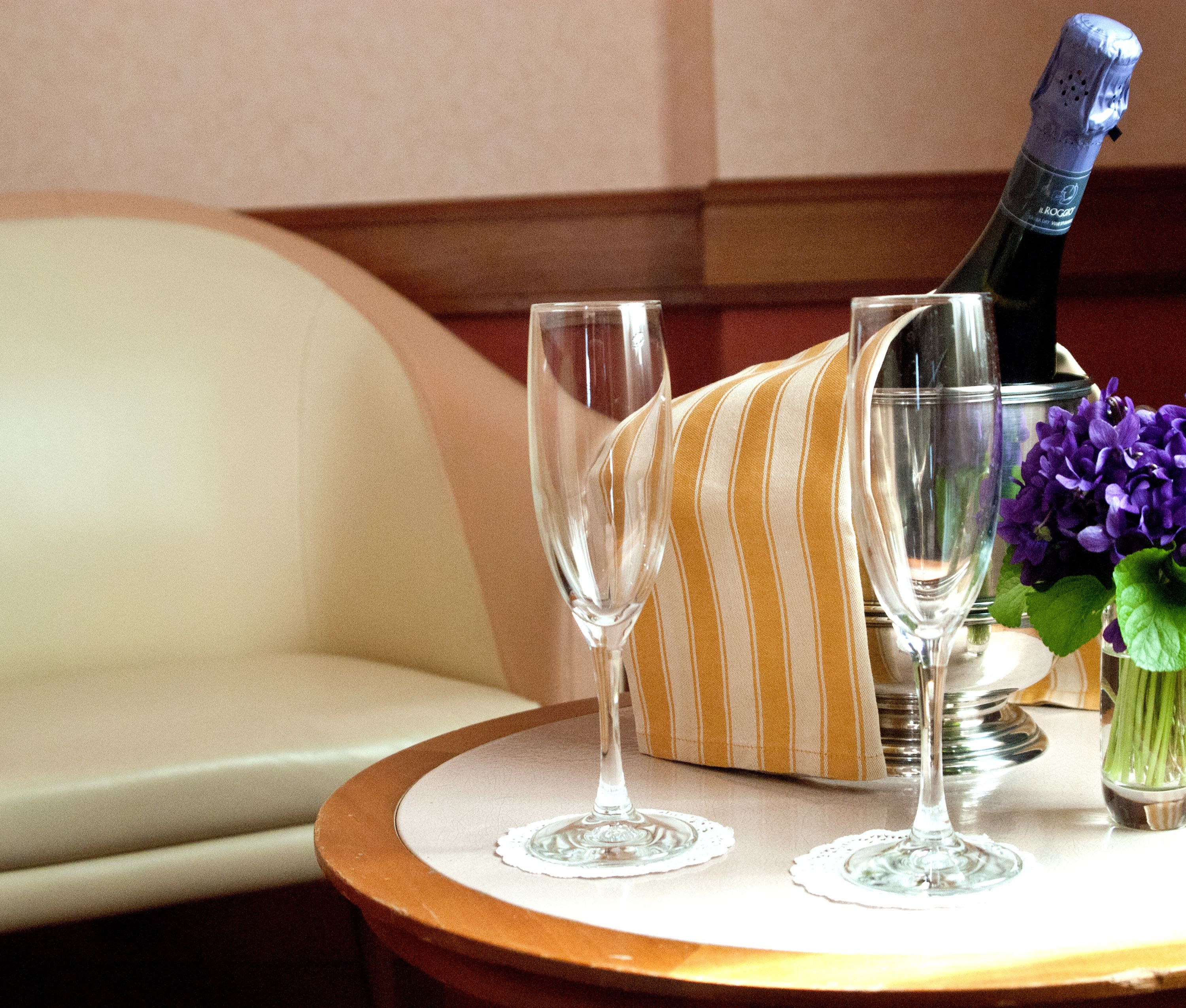 A table with a bottle of champagne, two glasses, and a vase with purple flowers.