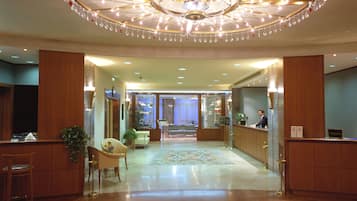 Eine Hotelhalle mit einem prunkvollen Kronleuchter, einer Rezeption und einer Sitzecke mit einem gemusterten Teppich.