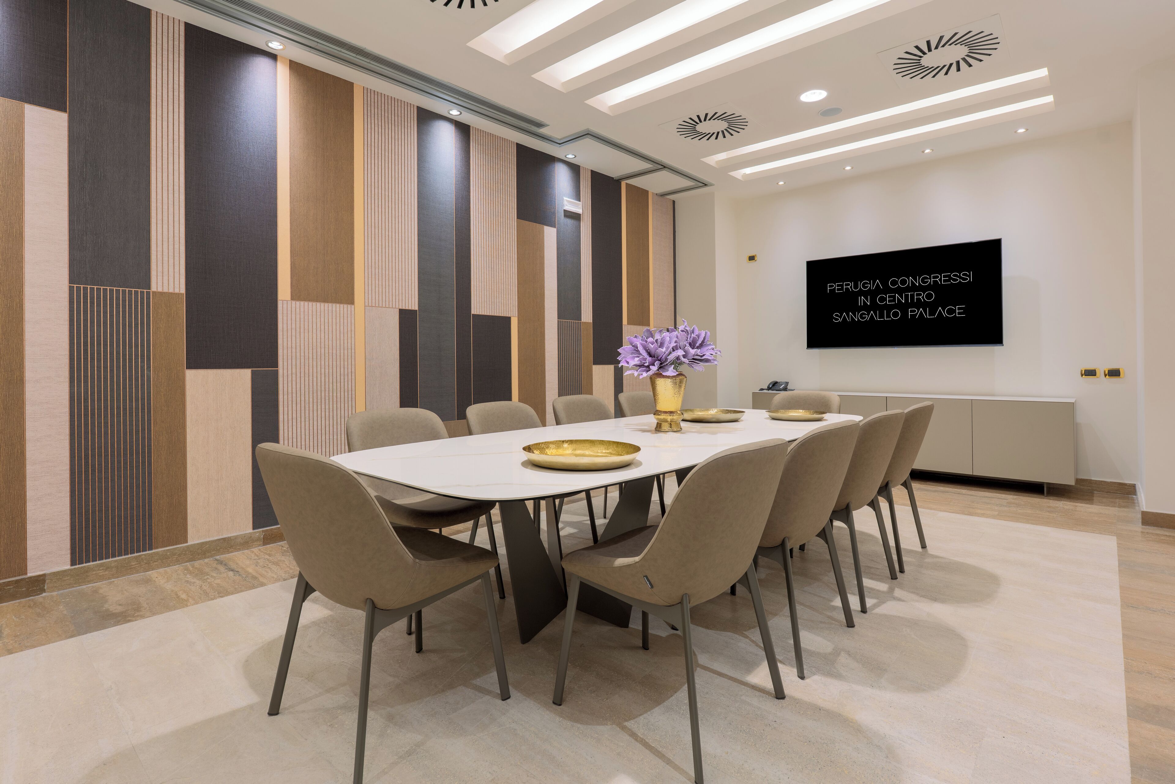 A modern conference room with a long table, beige chairs, and a decorative vase with purple flowers.