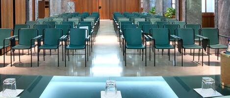 A conference room with rows of green chairs, a large table at the front, and marble walls.