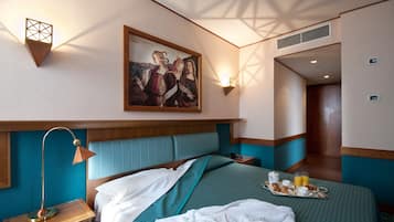 A hotel room with a bed, a bedside table, a lamp, a painting on the wall, and a tray with breakfast items.
