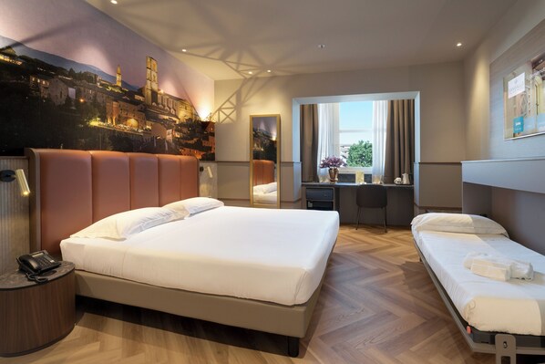 A hotel room with a large bed, a desk, a chair, a mirror, and a view of a cityscape. - Hotel Sangallo Palace (Perugia)