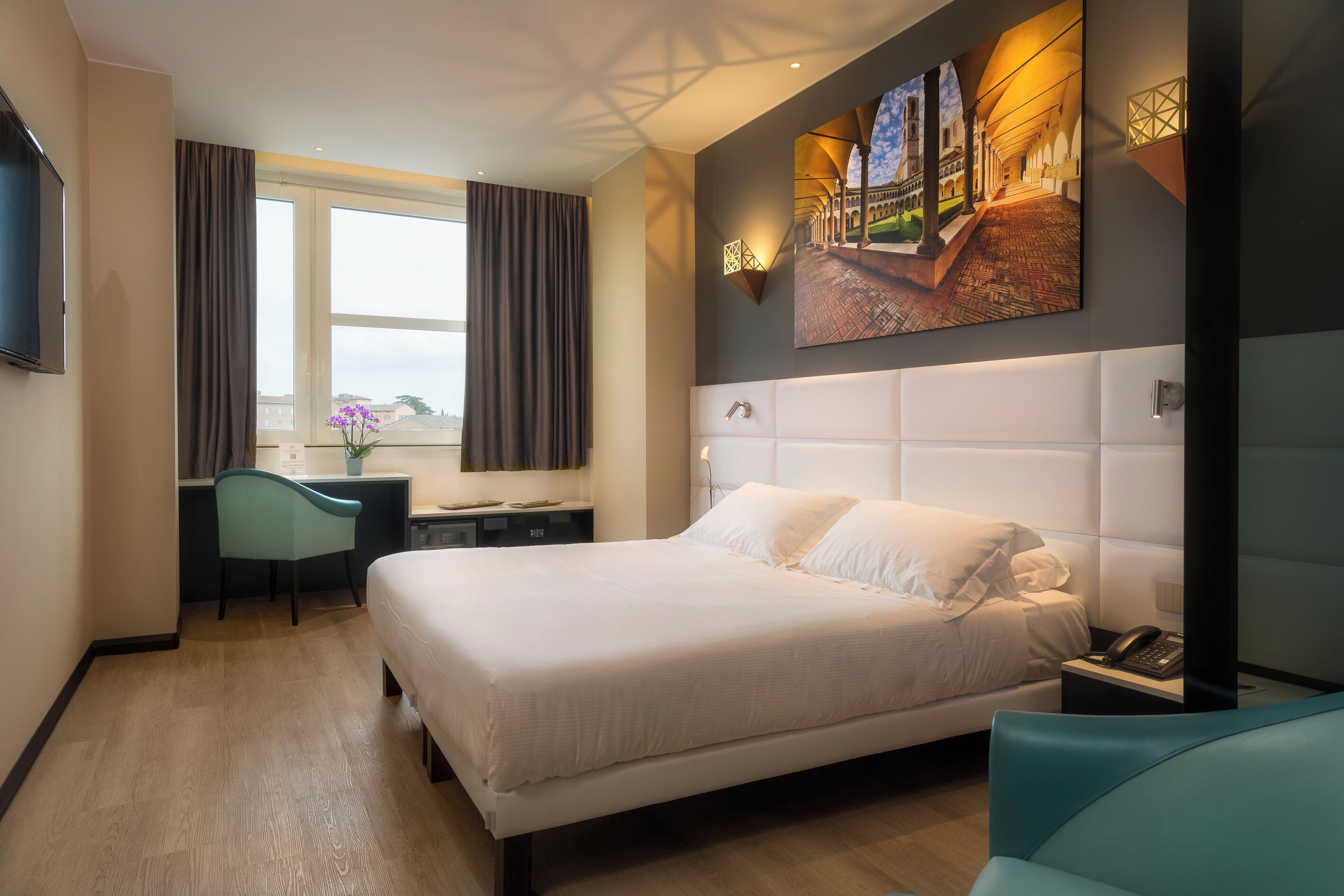 Una habitación de hotel con una cama grande, un escritorio, una silla, un televisor y un cuadro en la pared.