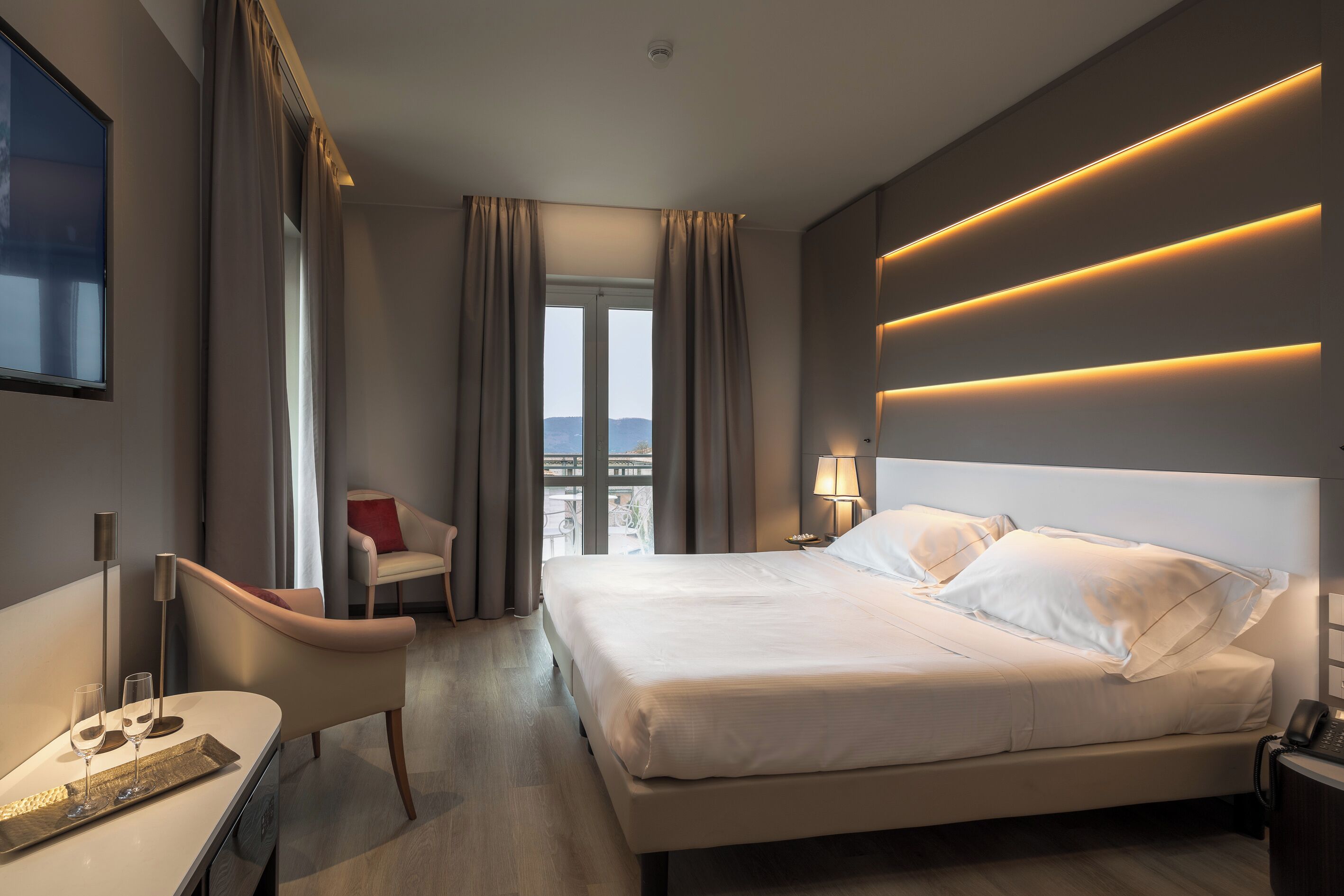 Una habitación de hotel moderna con una cama grande, un escritorio con lámpara, una silla y vistas a la ciudad por la ventana.