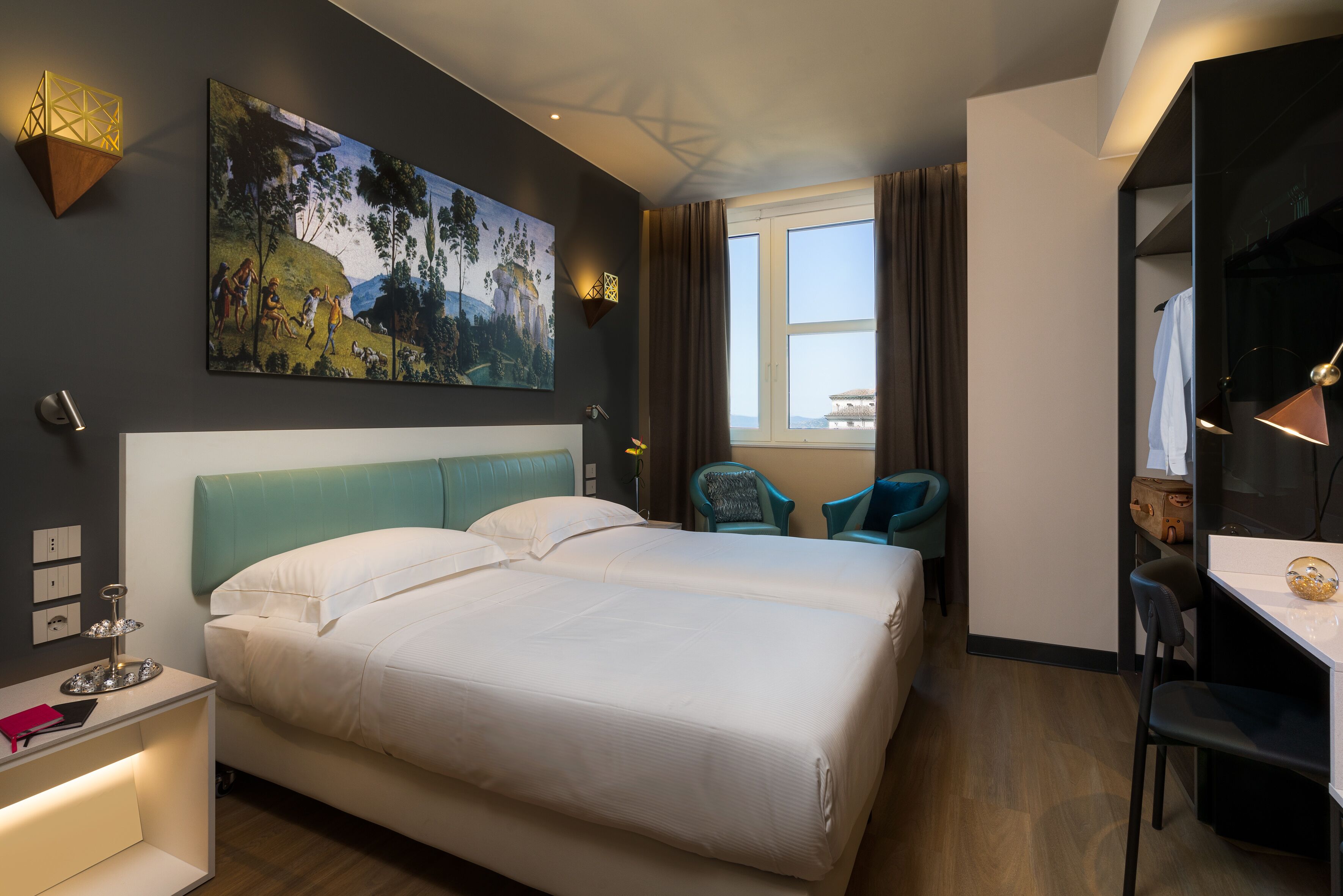 A modern hotel room with a large bed, a desk, and a chair. There is a painting on the wall and a window with curtains.