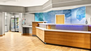 Un espace d’accueil comprenant un comptoir de réception en bois, un panneau d’information bleu et un réfrigérateur contenant des boissons.