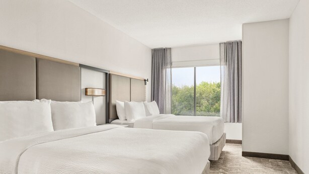 Une chambre d’hôtel avec deux lits, une grande fenêtre avec des rideaux et une vue sur la verdure.