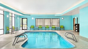Une piscine intérieure à l’eau d’un bleu limpide, entourée de chaises vertes et dotée d’un sol carrelé.