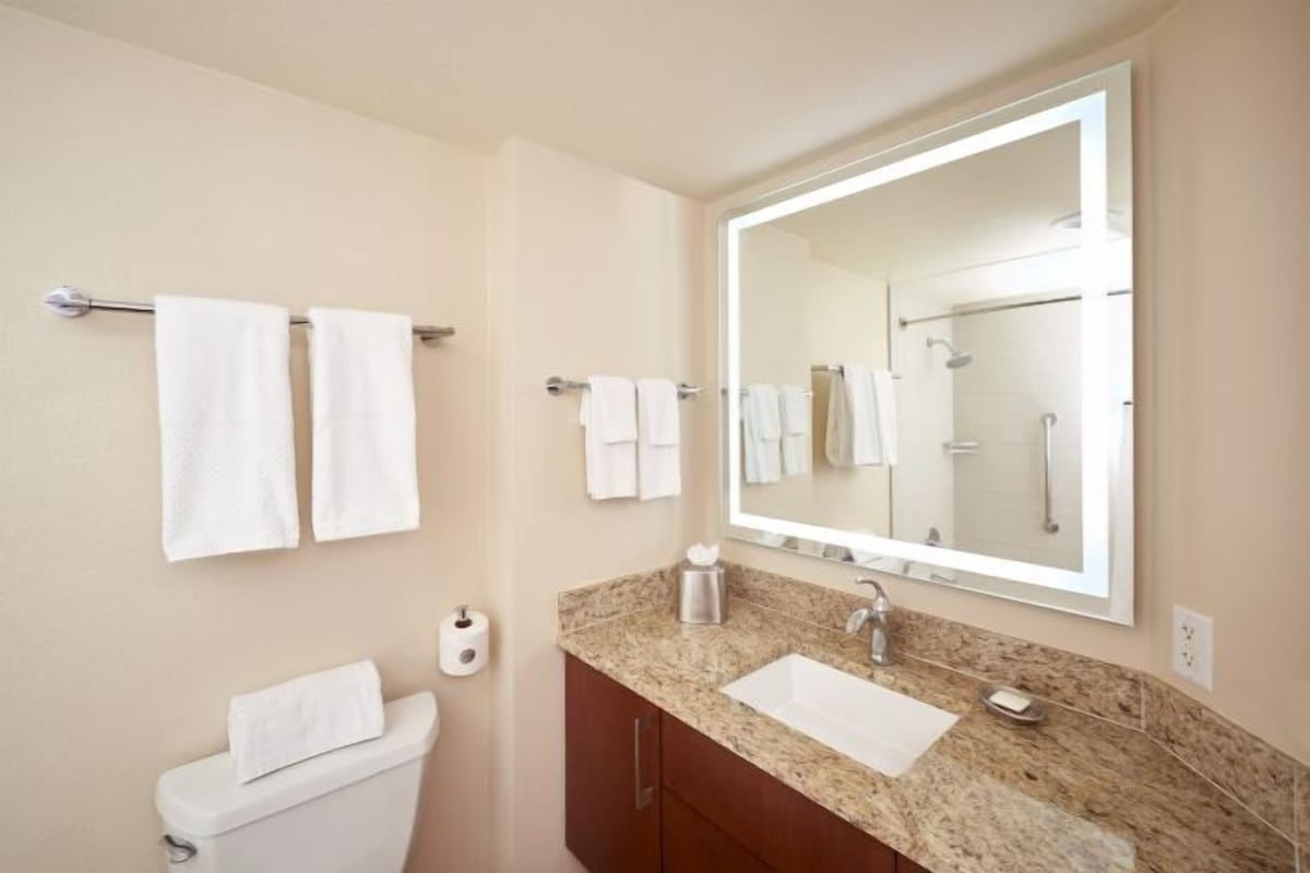 A bathroom with a toilet, sink, mirror, and towel rack.