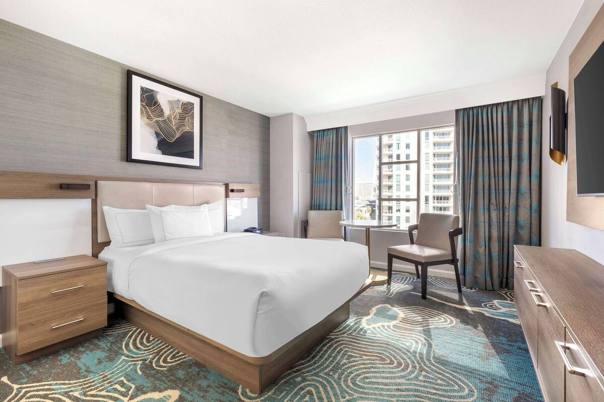 Habitación de hotel con una cama grande, escritorio, silla y vista a la ciudad.