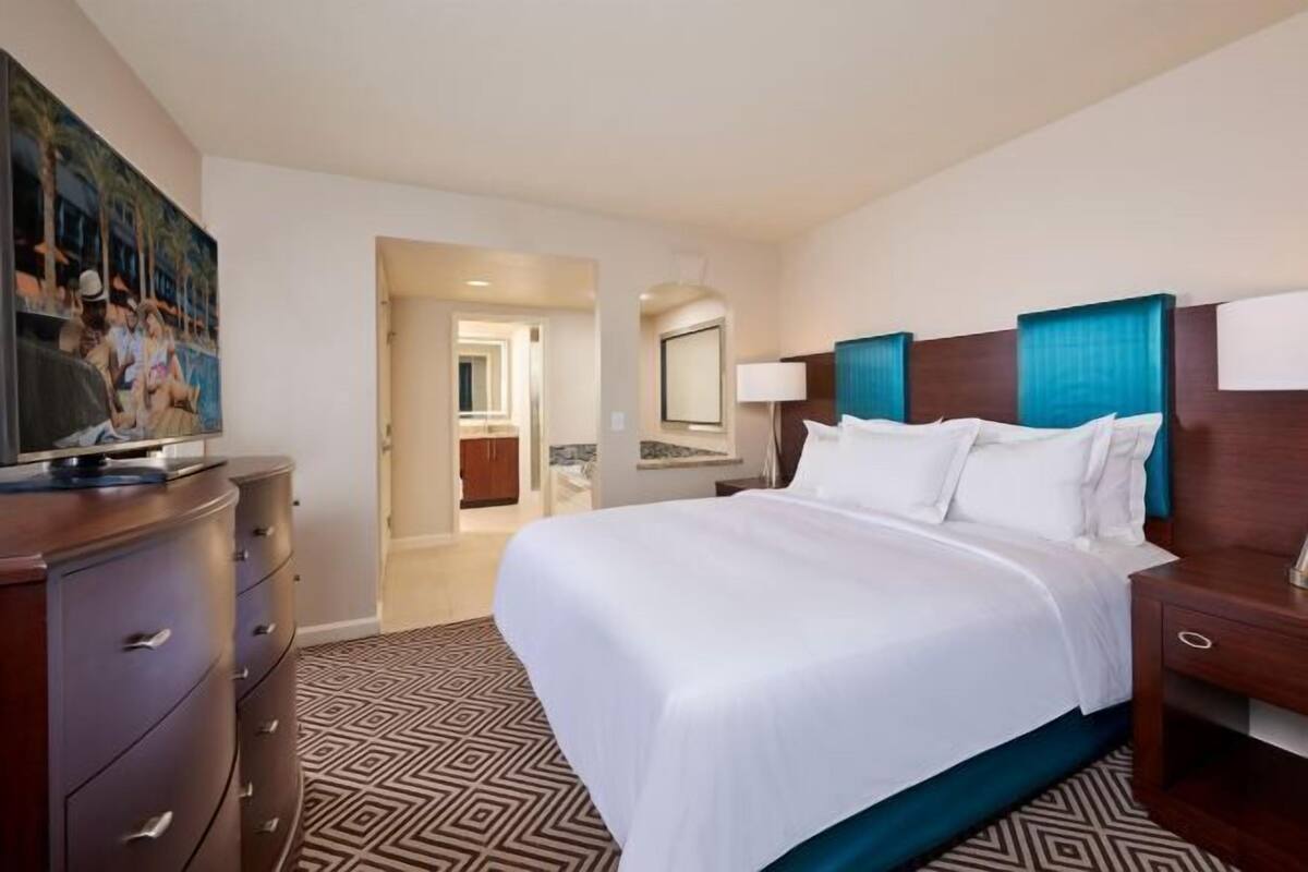 Habitación de hotel con una cama grande, cómoda, televisión y baño visible a través de una puerta abierta.