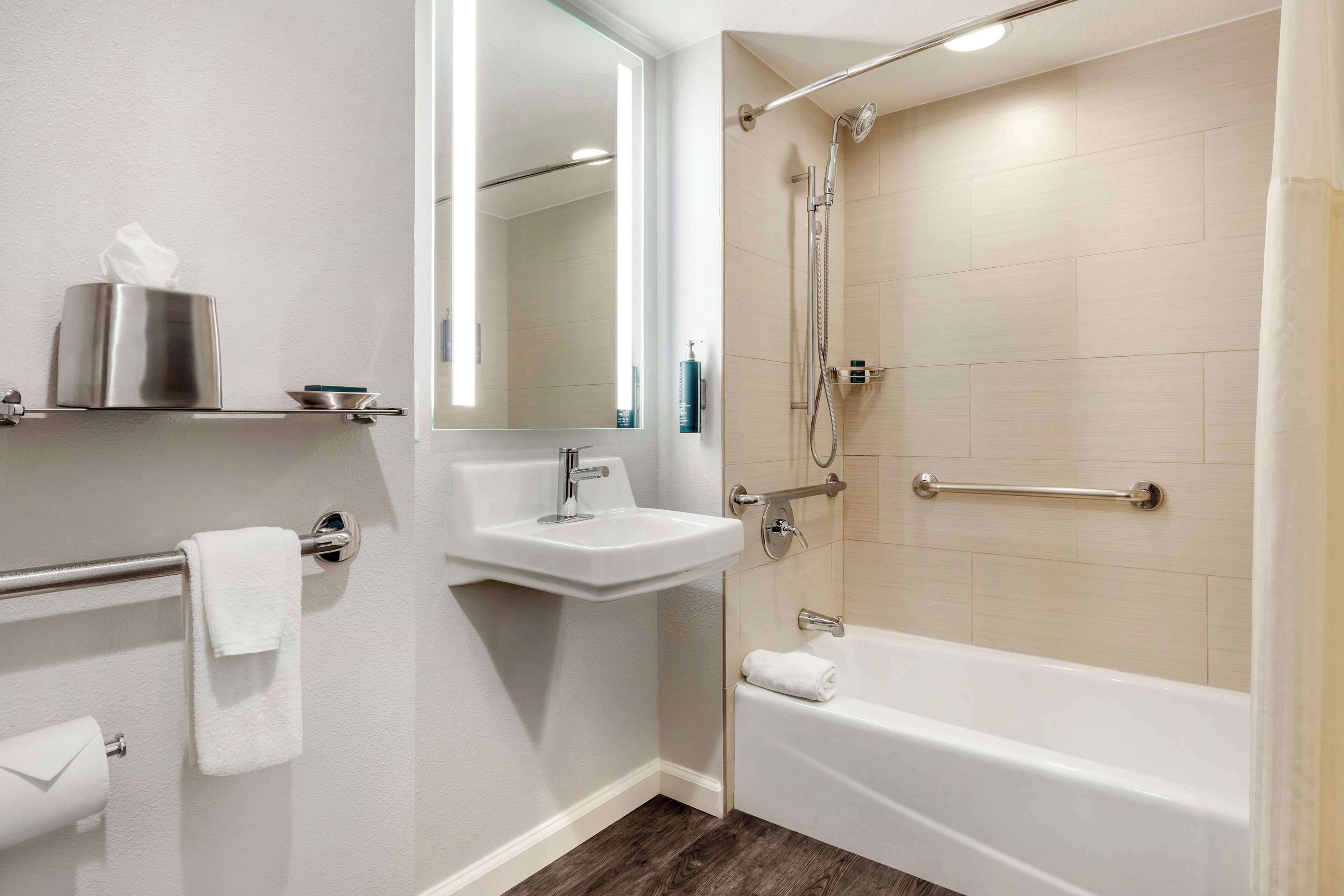 Un bagno moderno con lavandino, specchio, portasciuga, carta igienica e una vasca da bagno.