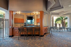 A bar area with a brick floor, wooden bar counter, and metal chairs.