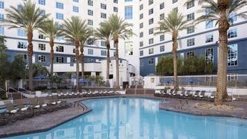 A hotel pool area with multiple lounge chairs and palm trees.