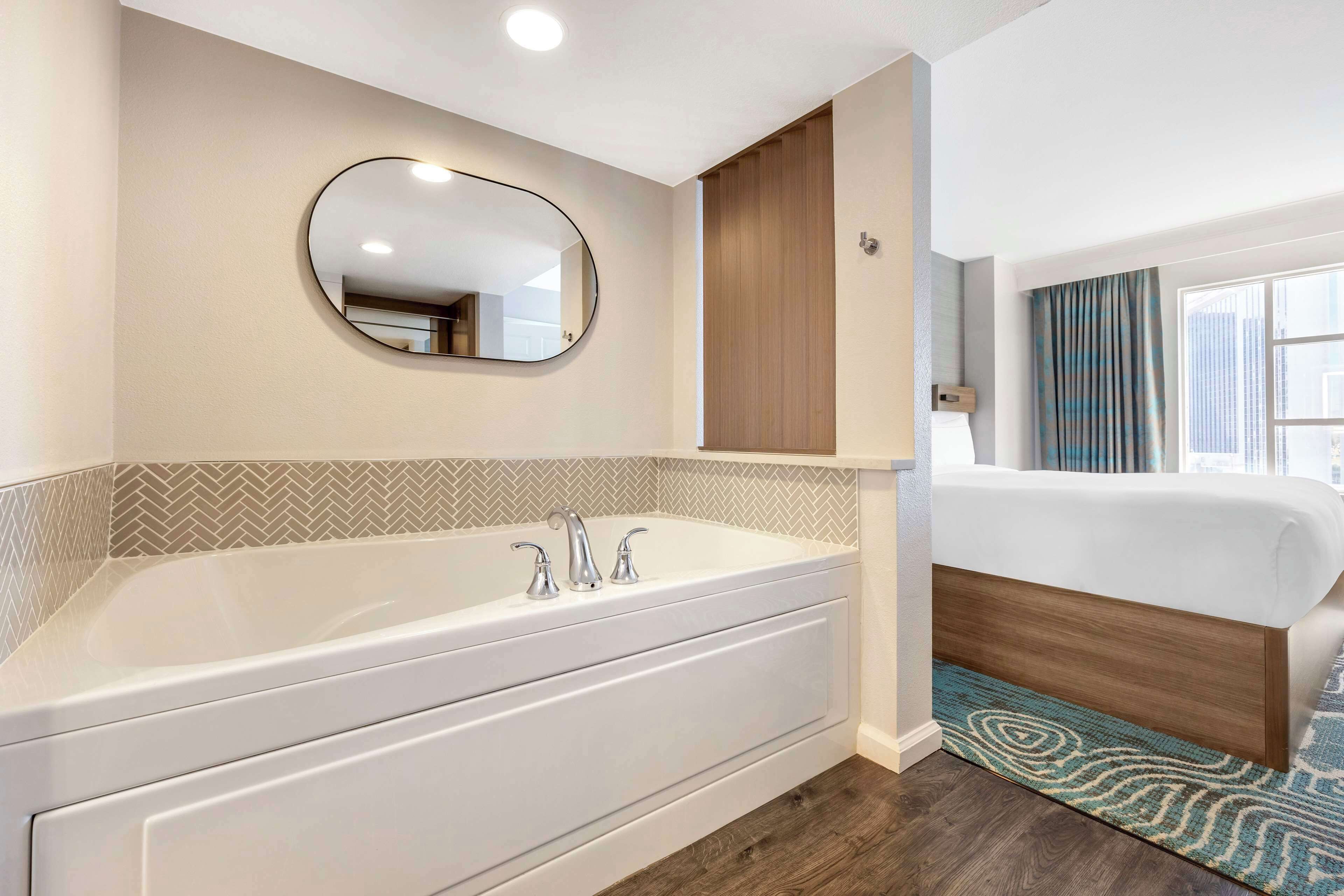Un baño moderno con una bañera independiente, un espejo redondo y un armario de madera.