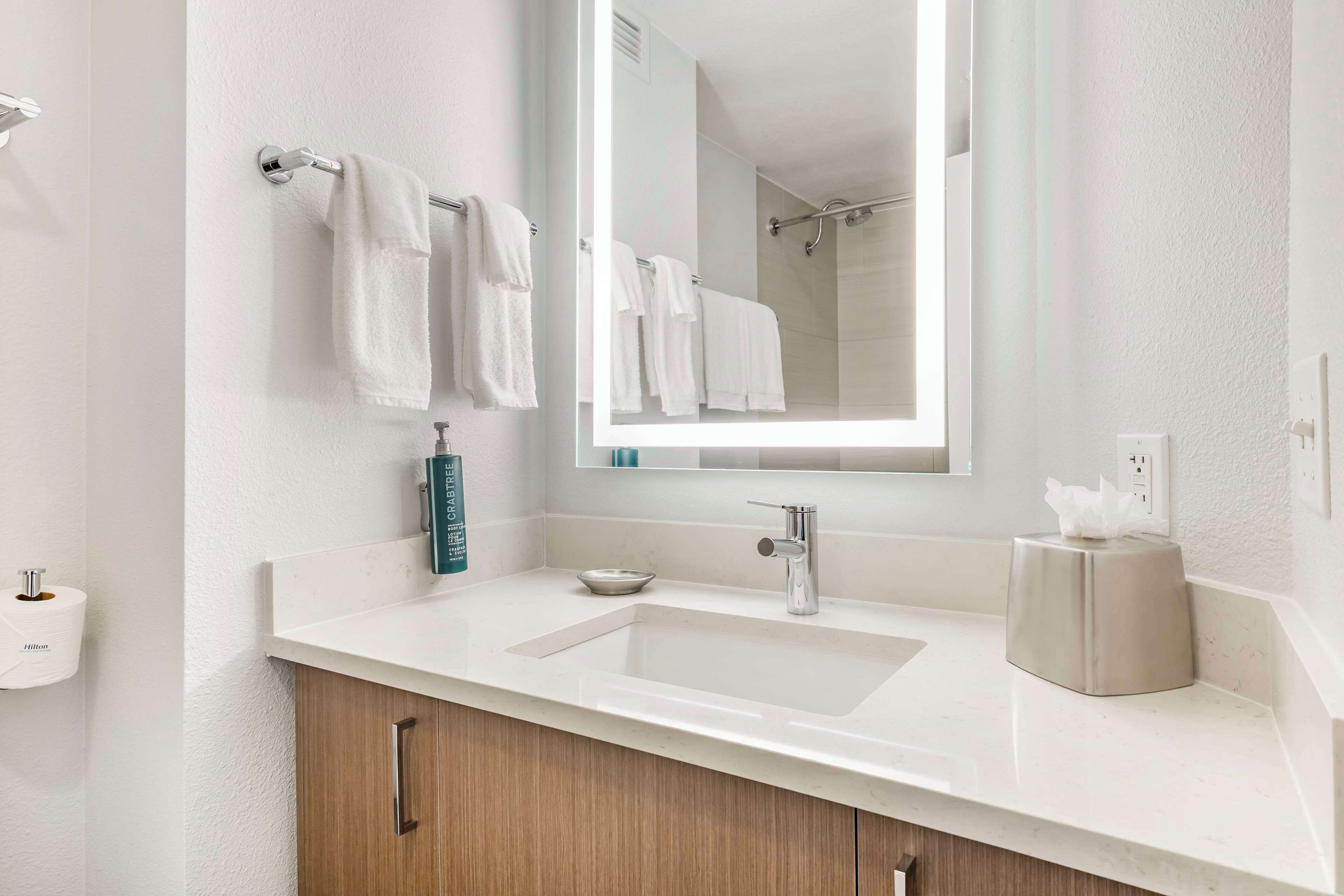 Une salle de bain moderne avec un lavabo blanc, un grand miroir et un porte-serviettes muni de plusieurs serviettes.
