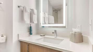 Une salle de bain moderne avec un lavabo blanc, un grand miroir et un porte-serviettes muni de plusieurs serviettes.