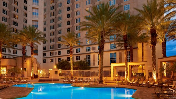 A hotel with a large pool surrounded by palm trees and lounge chairs.