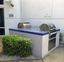 An outdoor grill area with a tiled countertop, a built-in oven, and a sign indicating BBQ tools are available at the deli.