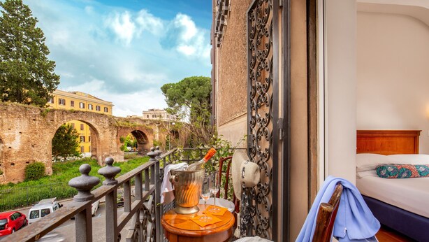 Ein Balkon mit Blick auf eine historische Brücke, ein Tisch mit einem Getränk und ein Bett mit einem Holz-Polsterkopfteil.