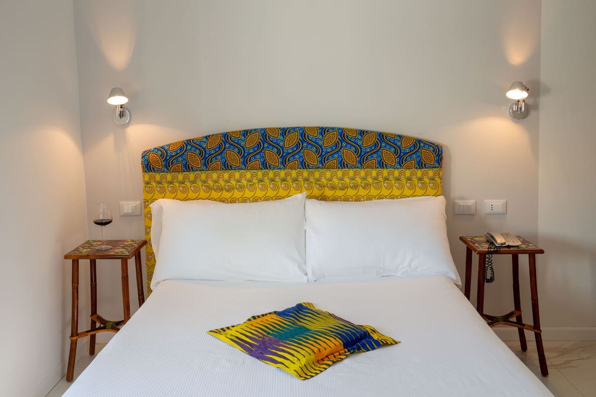 A bed with a patterned headboard, white pillows, and a colorful throw. There are two bedside tables with lamps and a wine glass on one.