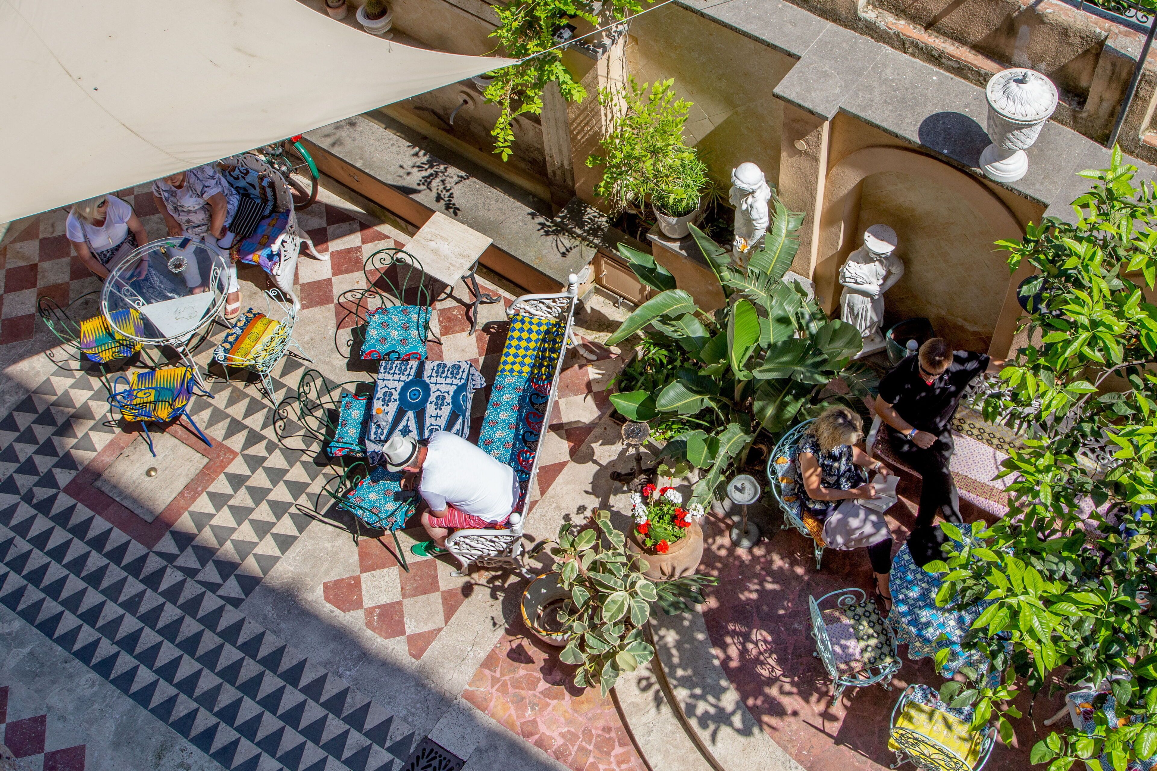 Une terrasse extérieure dotée d’un sol à motifs, de mobilier en métal et de plantes en pot.