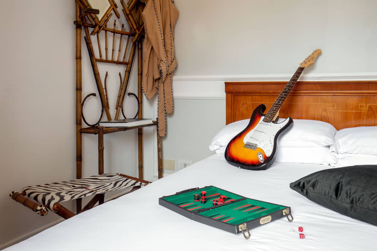 A bed with a guitar, a board game, and a chair.
