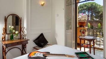 A room with a bed, a guitar, a green board game, a mirror, a vase with flowers, and a view of a tree and a bridge outside.