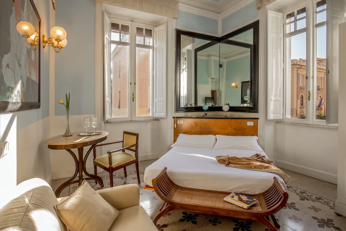 A hotel room with a bed, a chair, a small table, and a large mirror.