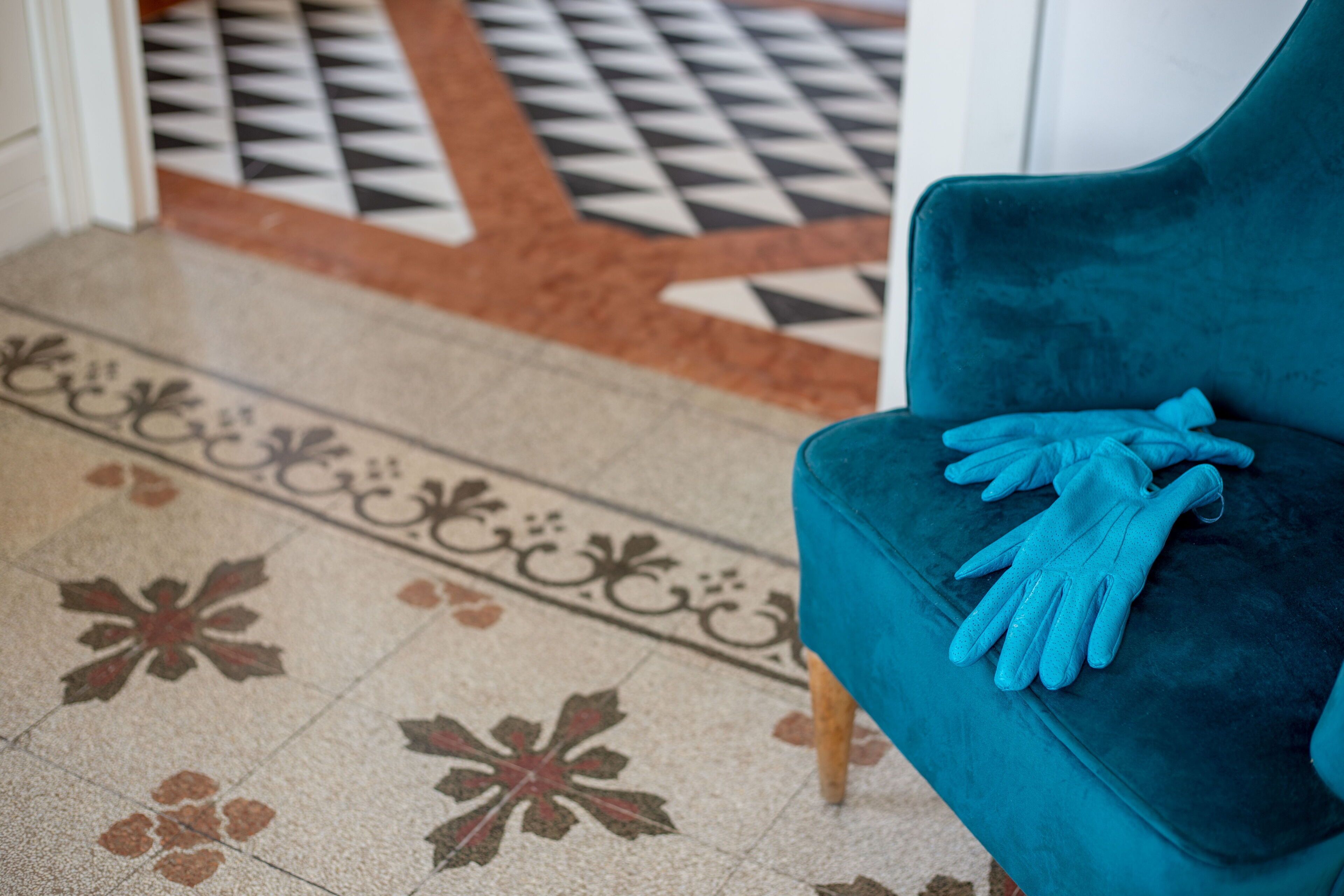 Ein türkisfarbener Sessel mit einer blauen Tagesdecke, platziert neben einem Fußboden mit geometrischen und floralen Mustern.