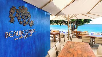 A beachfront restaurant with outdoor seating, a blue wall with a turtle mural, and a view of the sea.