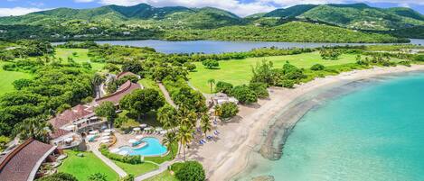 A resort with a beach, a swimming pool, and lush greenery.