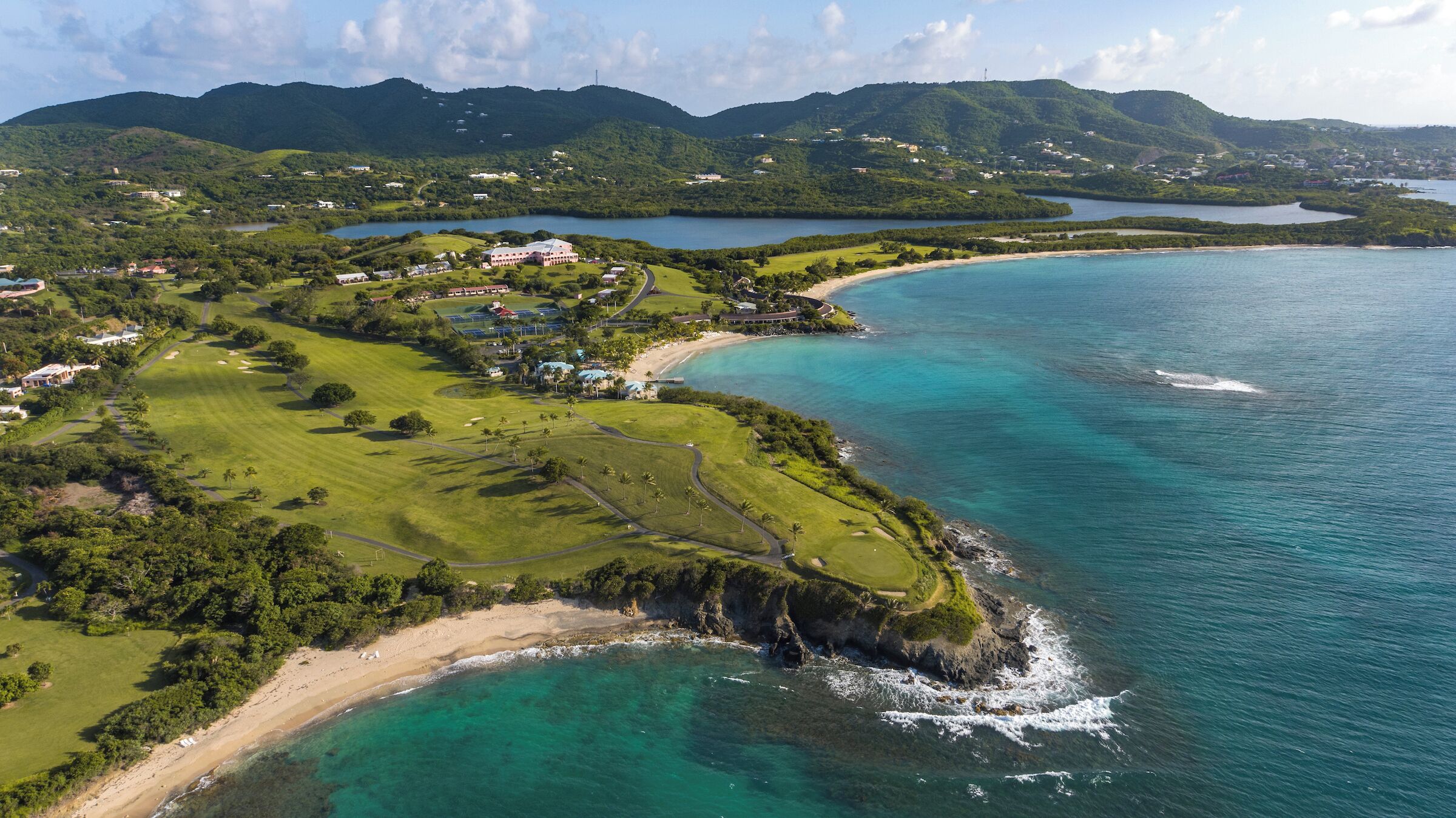 Vue aérienne d’une zone côtière comprenant un terrain de golf, une plage et une baie.