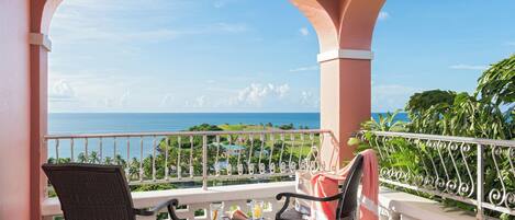 A balcony with two chairs, a small table, and a view of the ocean.
