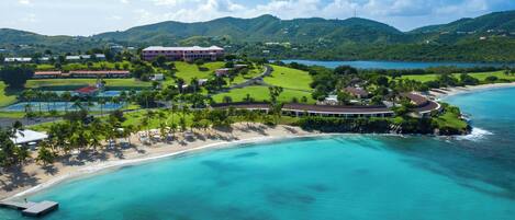An aerial view of a resort with a beach, a golf course, and a large building.