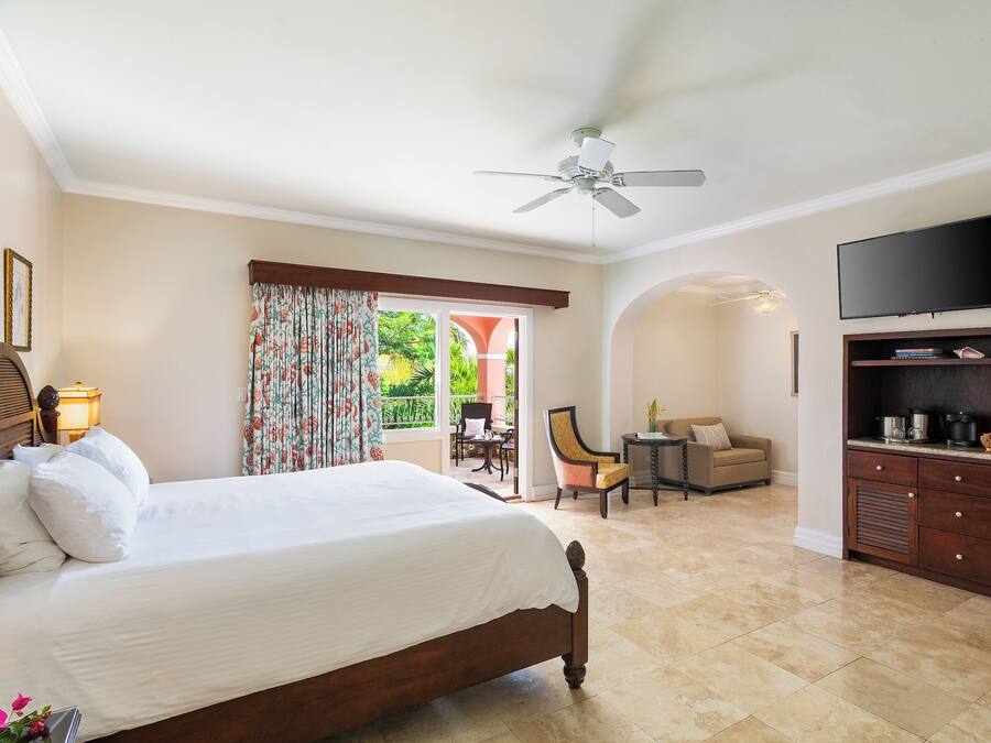 Ein Hotelzimmer mit einem großen Bett, einem Deckenventilator, einem Fernseher, einem kleinen Tisch, einem Sessel und Blick ins Freie.