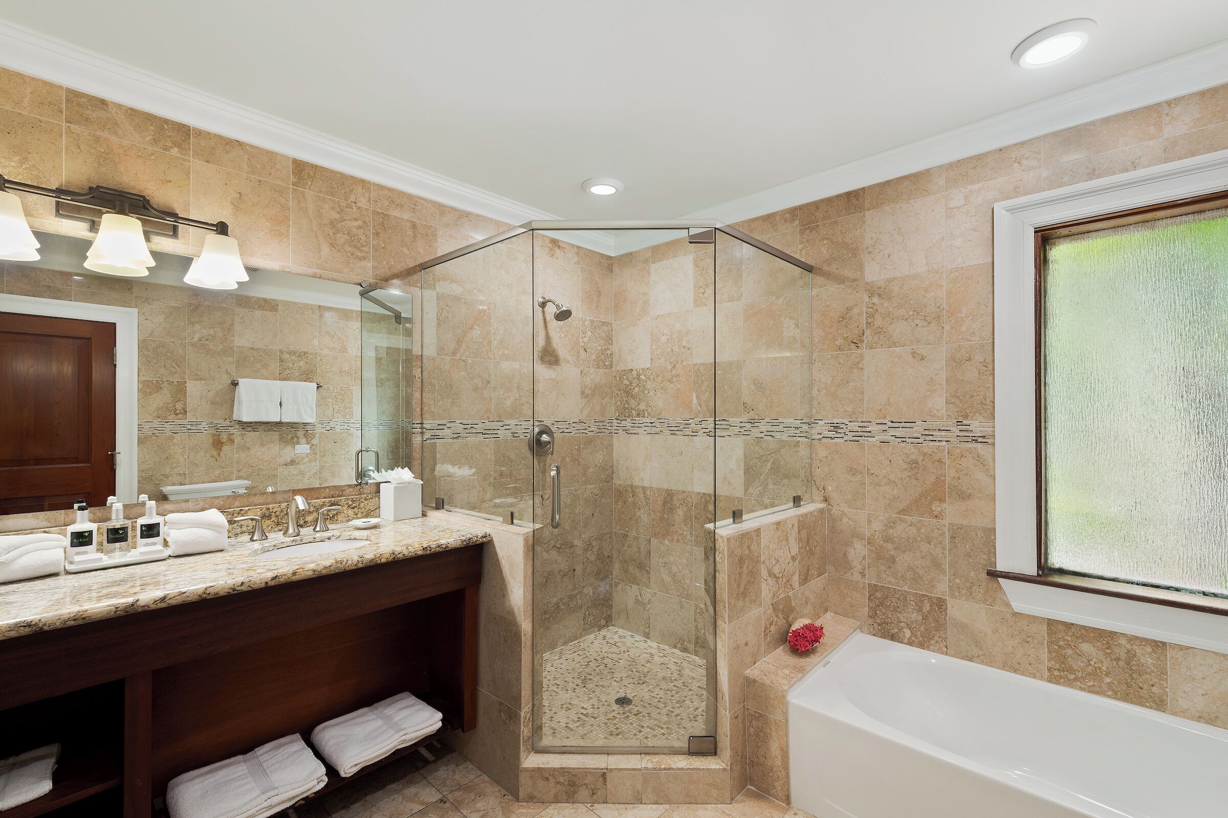 A modern bathroom with a glass-enclosed shower, a large bathtub, and a vanity with a mirror and multiple sinks.