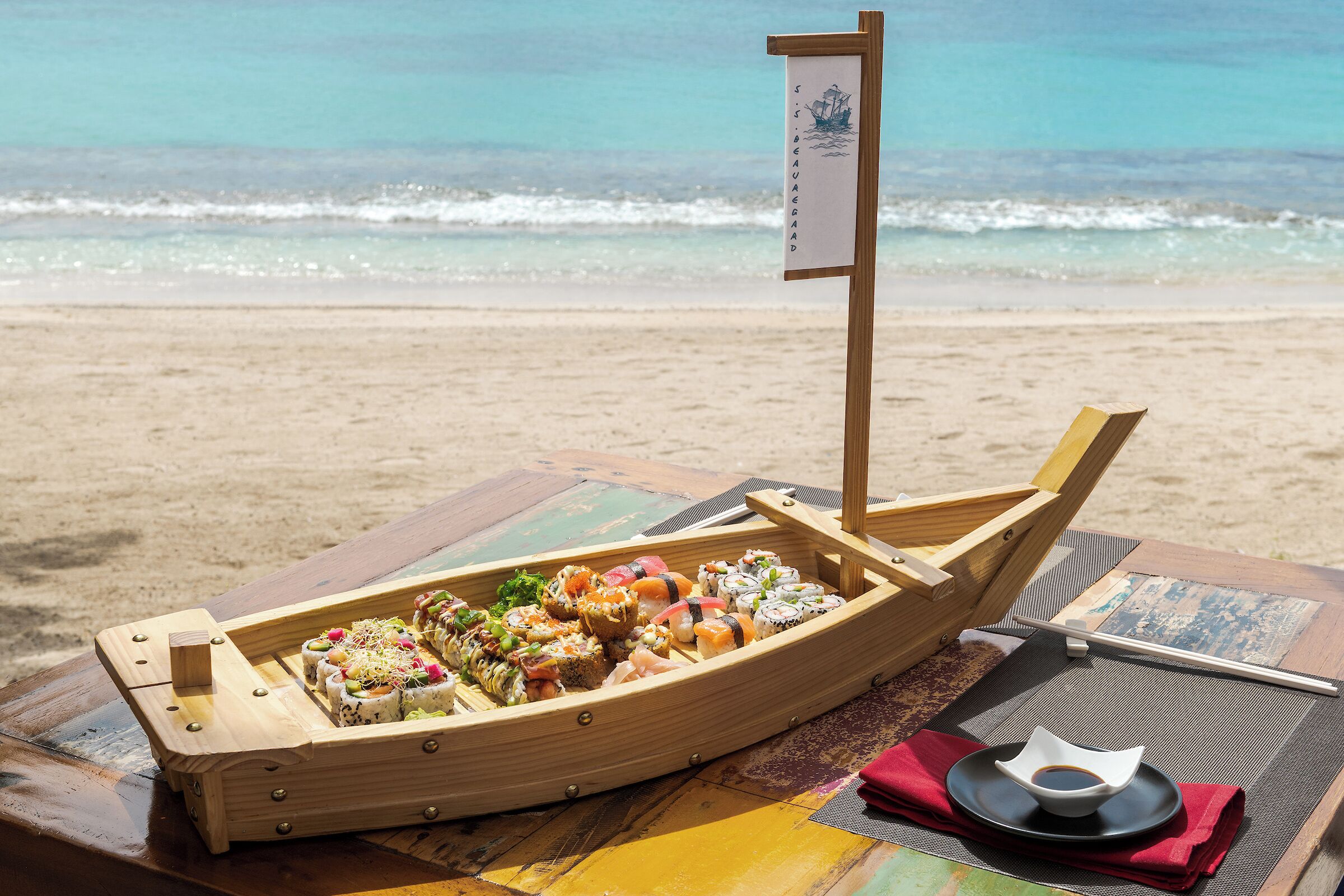 Ein hölzernes Boot, gefüllt mit Sushi, an einem Strand mit einer Flagge.