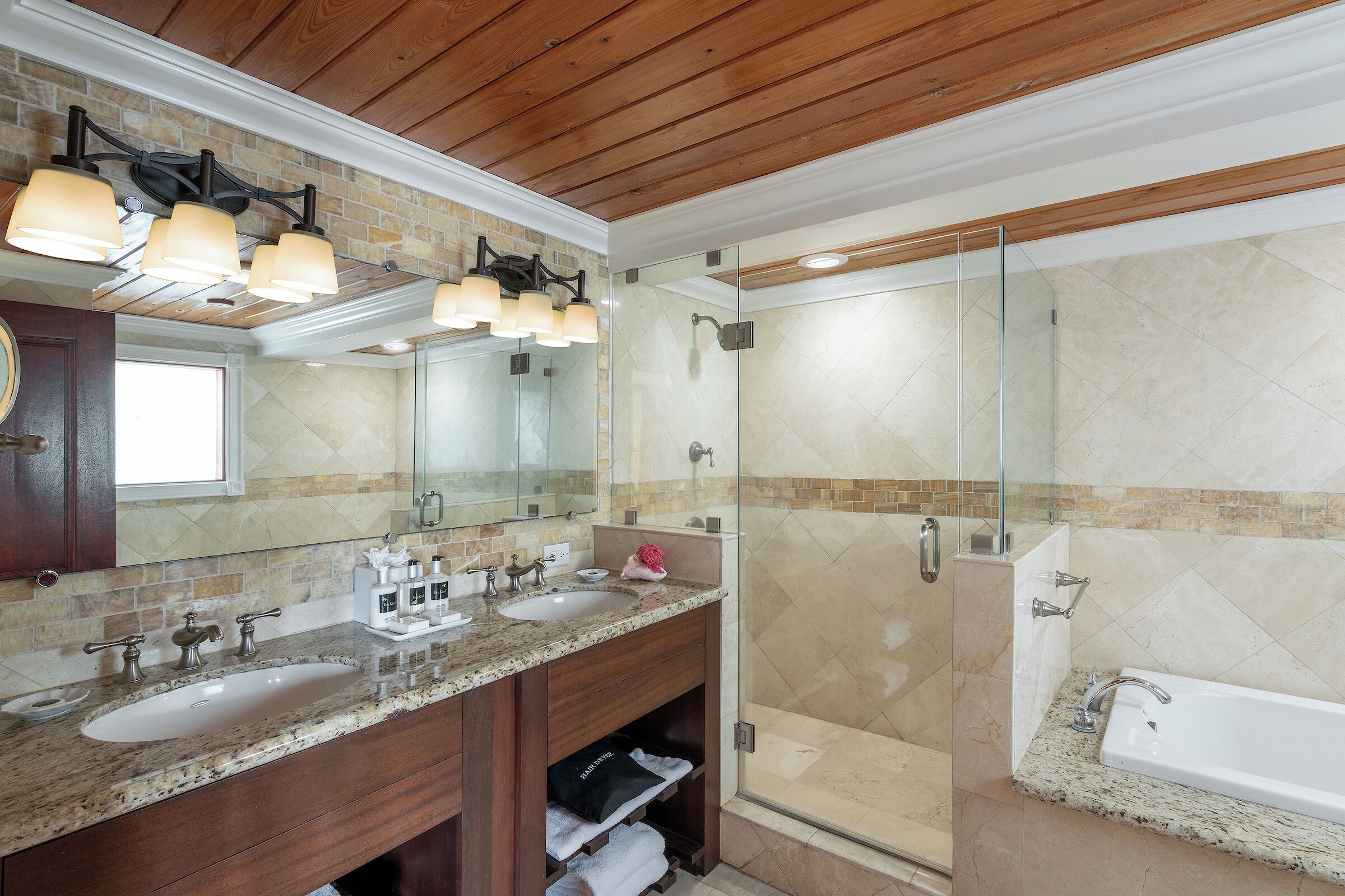 Un baño con dos lavamanos, un espejo grande y una ducha con mampara de vidrio.