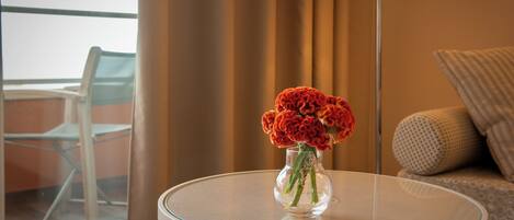 Ein runder Glastisch mit einer klaren Vase, in der Blumen, eine Lampe und ein Blick auf einen Balkon mit einem Stuhl sind.