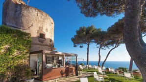 A coastal bar with outdoor seating, a stone tower, and a view of the sea.