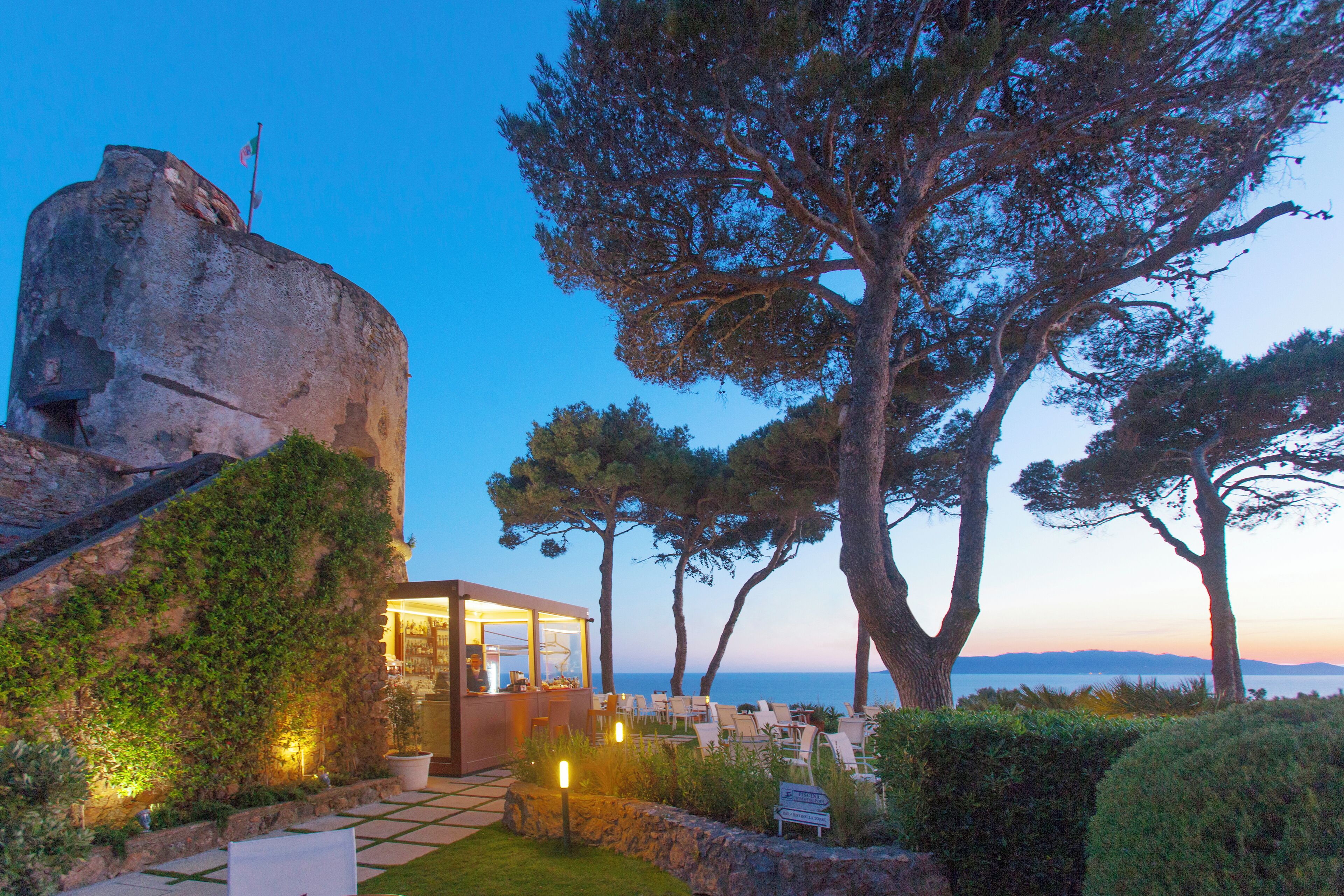 A coastal hotel with a large rock formation, outdoor seating area, and a view of the sea.