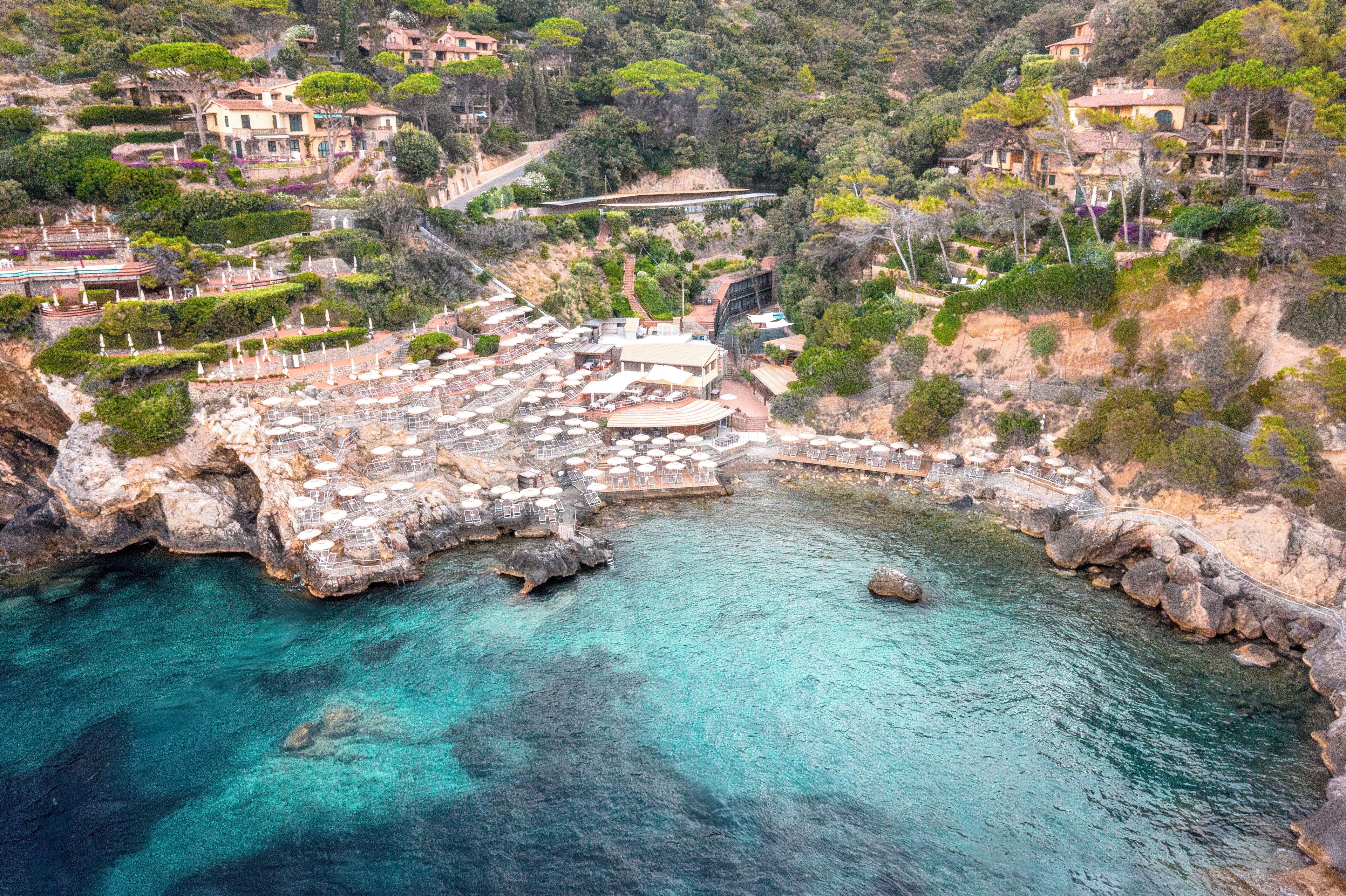 A coastal resort with multiple buildings, a rocky shoreline, and clear turquoise waters.